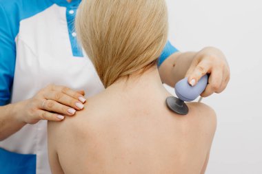 Genç bir kadın modern bir klinikte elektromanyetik terapi görüyor. Tedavi dokuların iyileşmesini hızlandırır, acıyı hafifletir ve kas gelişimini hızlandırır, genel sağlığa katkıda bulunur..