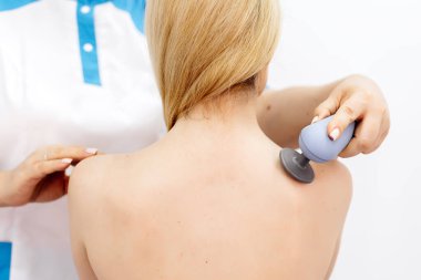 Genç bir kadın modern bir klinikte elektromanyetik terapi görüyor. Tedavi dokuların iyileşmesini hızlandırır, acıyı hafifletir ve kas gelişimini hızlandırır, genel sağlığa katkıda bulunur..