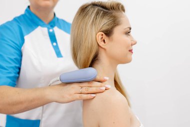Genç bir kadın modern bir klinikte elektromanyetik terapi görüyor. Tedavi dokuların iyileşmesini hızlandırır, acıyı hafifletir ve kas gelişimini hızlandırır, genel sağlığa katkıda bulunur..