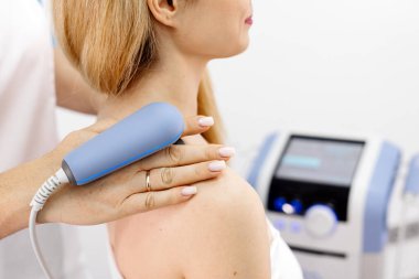 Genç bir kadın modern bir klinikte elektromanyetik terapi görüyor. Tedavi dokuların iyileşmesini hızlandırır, acıyı hafifletir ve kas gelişimini hızlandırır, genel sağlığa katkıda bulunur..