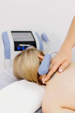 Genç bir kadın modern bir klinikte elektromanyetik terapi görüyor. Tedavi dokuların iyileşmesini hızlandırır, acıyı hafifletir ve kas gelişimini hızlandırır, genel sağlığa katkıda bulunur..