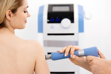 Fizyoterapist genç bir kadına şok dalgası terapisi uyguluyor. İyileşmeyi teşvik eden ve acıyı azaltan zararsız bir tedavi. Modern fizyoterapi tekniklerini ve tedavi yöntemlerini sergilemek için ideal..          