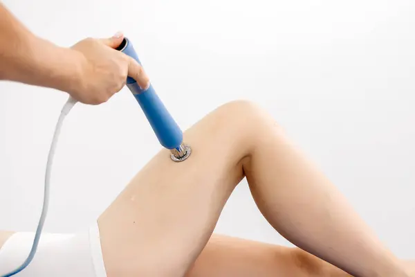 stock image Physiotherapist provides shockwave therapy to young woman. Non-invasive treatment that promotes healing and reduces pain. Ideal for showcasing modern physiotherapy techniques and recovery methods.          