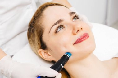 Modern klinikte genç bir kadına hidrojen soyarak tedavi uygulayan profesyonel bir kozmetik uzmanı. Derin cilt temizleme ve gençleştirme üzerine odaklanıyor. Gelişmiş cilt bakımı teknikleri için mükemmel..