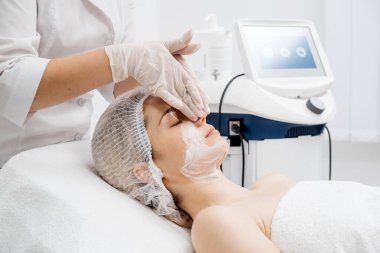 Kozmetik uzmanı modern bir güzellik kliniğinde gelişmiş cilt bakımı tekniklerini vurgulayan bir yüz kremi uyguluyor. Reklamınızda birinci sınıf spa tedavilerini sergilemek için ideal..     