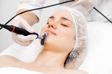 Kozmetik uzmanı modern bir klinikteki genç bir kadına radyasyon kaldırma uyguluyor. Bu gelişmiş işlem cilt bakımını sıkılaştırır ve gençleştirmeyi teşvik eder. Güzellik tedavileri için ideal..