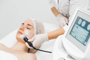 Kozmetik uzmanı modern bir klinikteki genç bir kadına radyasyon kaldırma uyguluyor. Bu gelişmiş işlem cilt bakımını sıkılaştırır ve gençleştirmeyi teşvik eder. Güzellik tedavileri için ideal..