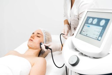 Kozmetik uzmanı modern bir klinikteki genç bir kadına radyasyon kaldırma uyguluyor. Bu gelişmiş işlem cilt bakımını sıkılaştırır ve gençleştirmeyi teşvik eder. Güzellik tedavileri için ideal..