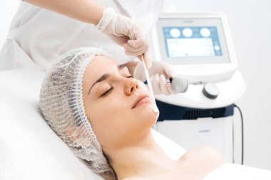 Kozmetik uzmanı modern bir klinikteki genç bir kadına radyasyon kaldırma uyguluyor. Bu gelişmiş işlem cilt bakımını sıkılaştırır ve gençleştirmeyi teşvik eder. Güzellik tedavileri için ideal..