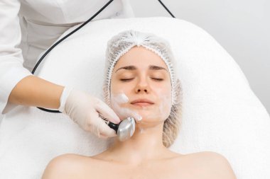 Kozmetik uzmanı modern bir klinikteki genç bir kadına radyasyon kaldırma uyguluyor. Bu gelişmiş işlem cilt bakımını sıkılaştırır ve gençleştirmeyi teşvik eder. Güzellik tedavileri için ideal..