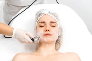 Kozmetik uzmanı modern bir klinikteki genç bir kadına radyasyon kaldırma uyguluyor. Bu gelişmiş işlem cilt bakımını sıkılaştırır ve gençleştirmeyi teşvik eder. Güzellik tedavileri için ideal..
