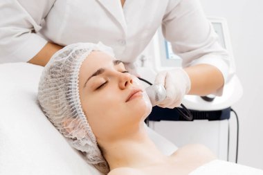 Kozmetik uzmanı modern bir klinikteki genç bir kadına radyasyon kaldırma uyguluyor. Bu gelişmiş işlem cilt bakımını sıkılaştırır ve gençleştirmeyi teşvik eder. Güzellik tedavileri için ideal..