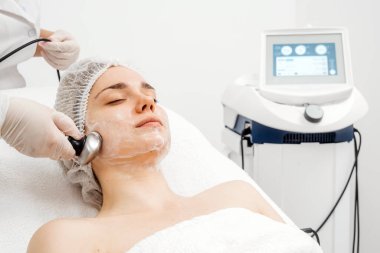 Kozmetik uzmanı modern bir klinikteki genç bir kadına radyasyon kaldırma uyguluyor. Bu gelişmiş işlem cilt bakımını sıkılaştırır ve gençleştirmeyi teşvik eder. Güzellik tedavileri için ideal..