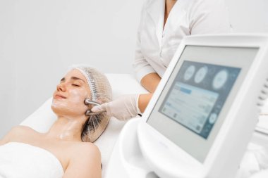 Kozmetik uzmanı yüz gençleştirme ve sıkma için RF kaldırma ameliyatı yapıyor. Bu müdahale etmeyen prosedür cildinizi sertleştirir ve pürüzsüzleştirir. Güzellik rutininizi geliştirir..