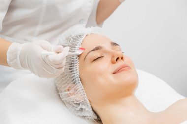 Kozmetik uzmanı modern bir güzellik kliniğinde gelişmiş cilt bakımı tekniklerini vurgulayan bir yüz kremi uyguluyor. Reklamınızda birinci sınıf spa tedavilerini sergilemek için ideal..     