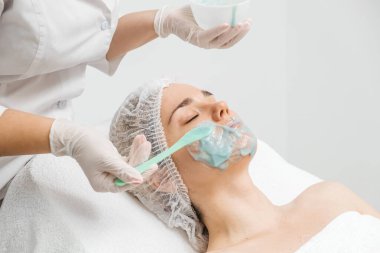 Kozmetik uzmanı modern bir kuaförde genç bir kadına aljinat maske takıyor.. 