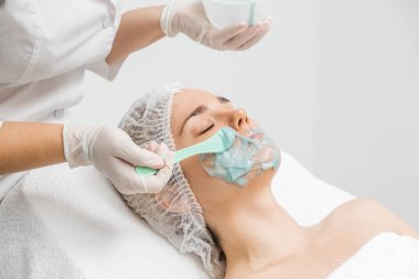 Kozmetik uzmanı modern bir kuaförde genç bir kadına aljinat maske takıyor.. 