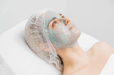 Modern bir güzellik kliniğinde yüz kremi kullanan genç bir kadın gelişmiş cilt bakımı tekniklerini ön plana çıkarıyor. Reklamınızda birinci sınıf spa tedavilerini sergilemek için ideal..     