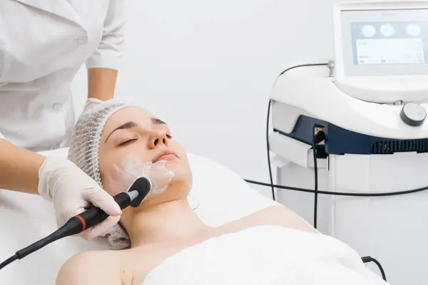 Kozmetik uzmanı modern bir klinikteki genç bir kadına radyasyon kaldırma uyguluyor. Bu gelişmiş işlem cilt bakımını sıkılaştırır ve gençleştirmeyi teşvik eder. Güzellik tedavileri için ideal..