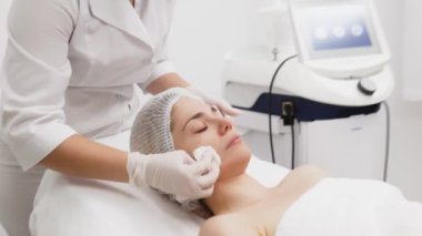 Kozmetik uzmanı modern bir güzellik kliniğinde gelişmiş cilt bakımı tekniklerini vurgulayan bir yüz kremi uyguluyor. Reklamınızda birinci sınıf spa tedavilerini sergilemek için ideal..     