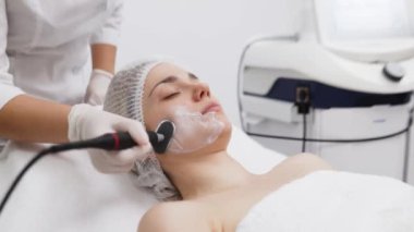 Kozmetik uzmanı modern bir klinikteki genç bir kadına radyasyon kaldırma uyguluyor. Bu gelişmiş işlem cilt bakımını sıkılaştırır ve gençleştirmeyi teşvik eder. Güzellik tedavileri için ideal..
