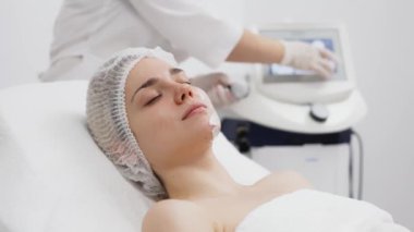 Kozmetik uzmanı modern bir klinikteki genç bir kadına radyasyon kaldırma uyguluyor. Bu gelişmiş işlem cilt bakımını sıkılaştırır ve gençleştirmeyi teşvik eder. Güzellik tedavileri için ideal..
