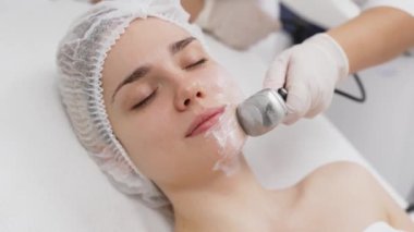 Kozmetik uzmanı modern bir klinikteki genç bir kadına radyasyon kaldırma uyguluyor. Bu gelişmiş işlem cilt bakımını sıkılaştırır ve gençleştirmeyi teşvik eder. Güzellik tedavileri için ideal..