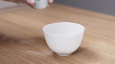 Kadın elleri koruyucu eldivenlerle kaseye pudra koyuyor.