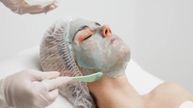 Kozmetik uzmanı modern bir kuaförde genç bir kadına aljinat maske takıyor.. 