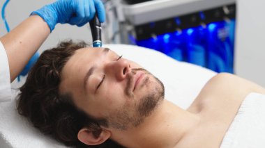 Adam güzellik kliniğinde yüz bakımı görüyor. Bu gelişmiş prosedür cildinizi gençleştirir ve canlandırır. Reklamlarınızda kaliteli cilt bakımı için idealdir..