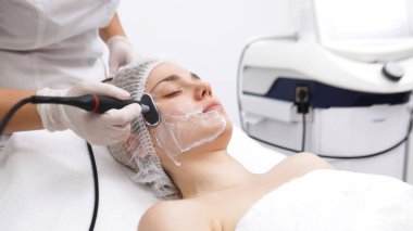 Kozmetik uzmanı, modern bir klinikteki genç bir kadına radyoterapi uyguluyor.. 