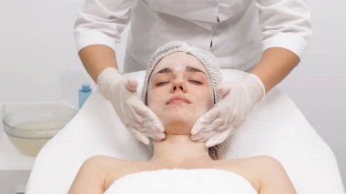 Kozmetik uzmanı genç bir kadının yüzünü modern bir güzellik salonunda özel ürünlerle temizliyor.. 