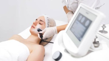 Kozmetik uzmanı, modern bir klinikteki genç bir kadına radyoterapi uyguluyor.. 