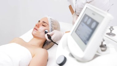 Kozmetik uzmanı, modern bir klinikteki genç bir kadına radyoterapi uyguluyor.. 