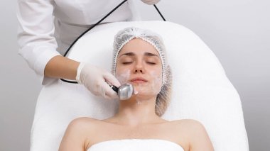 Kozmetik uzmanı modern bir klinikteki genç bir kadına radyasyon kaldırma uyguluyor. Bu gelişmiş işlem cilt bakımını sıkılaştırır ve gençleştirmeyi teşvik eder. Güzellik tedavileri için ideal..