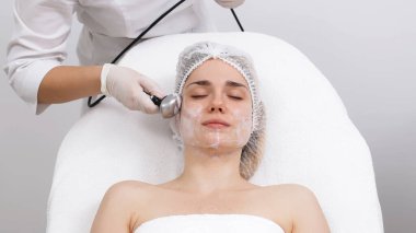 Kozmetik uzmanı modern bir klinikteki genç bir kadına radyasyon kaldırma uyguluyor. Bu gelişmiş işlem cilt bakımını sıkılaştırır ve gençleştirmeyi teşvik eder. Güzellik tedavileri için ideal..