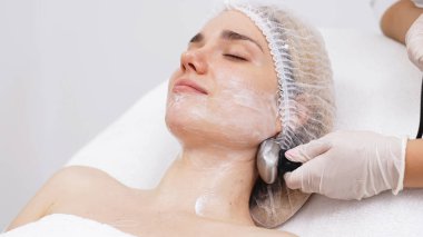 Cosmetologist applies radiofrequency lifting to a young woman in a modern clinic. This advanced procedure tightens skin and promotes rejuvenation, ideal for showcasing beauty treatments. clipart