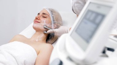 Kozmetik uzmanı yüz gençleştirme ve sıkma için RF kaldırma ameliyatı yapıyor. Bu müdahale etmeyen prosedür cildinizi sertleştirir ve pürüzsüzleştirir. Güzellik rutininizi geliştirir..