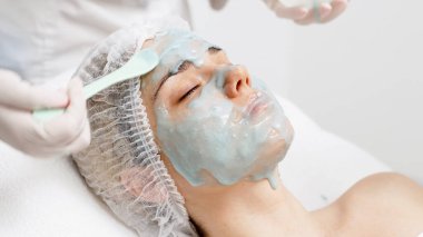 Bir kozmetik uzmanı modern bir kuaförde genç bir kadına aljinat maske takıyor.. 