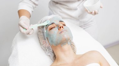 Bir kozmetik uzmanı modern bir kuaförde genç bir kadına aljinat maske takıyor.. 