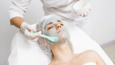 Bir kozmetik uzmanı modern bir kuaförde genç bir kadına aljinat maske takıyor.. 
