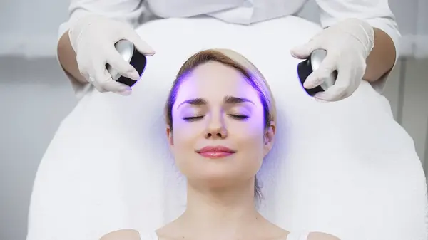 Kozmetik uzmanı yüz gençleştirme için LED ışık terapisi uyguluyor. Bu zararsız tedavi cilt esnekliğini arttırır, yaşlanma belirtilerini azaltır ve cilt parlaklığını arttırır..