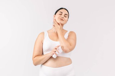 Stüdyoda kozmetik krem şişesiyle poz veren beyaz bir kadın.