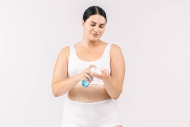 Stüdyoda kozmetik krem şişesiyle poz veren beyaz bir kadın.