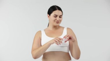 Genç beyaz bir kadın stüdyoda ellerine krem sürüyor.