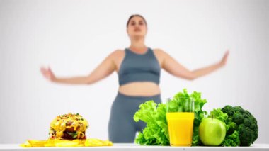 Hamburger sağlıklı gıdaya karşı, diyet konsepti, bulanık arka planda egzersiz yapan genç, kıvrımlı kadın.