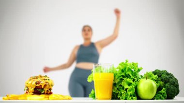 Hamburger sağlıklı gıdaya karşı, diyet konsepti, bulanık arka planda egzersiz yapan genç, kıvrımlı kadın.