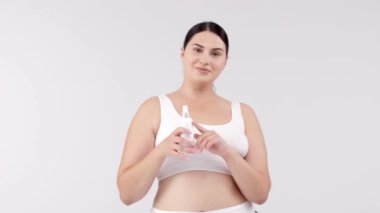 Stüdyoda vücuduna kozmetik sıvısı sıkan beyaz bir kadın.