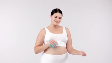 Genç beyaz bir kadın stüdyoda ellerine krem sürüyor.