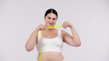 Kilolu bir kadın beyaz arka planda mezurayla poz veriyor.